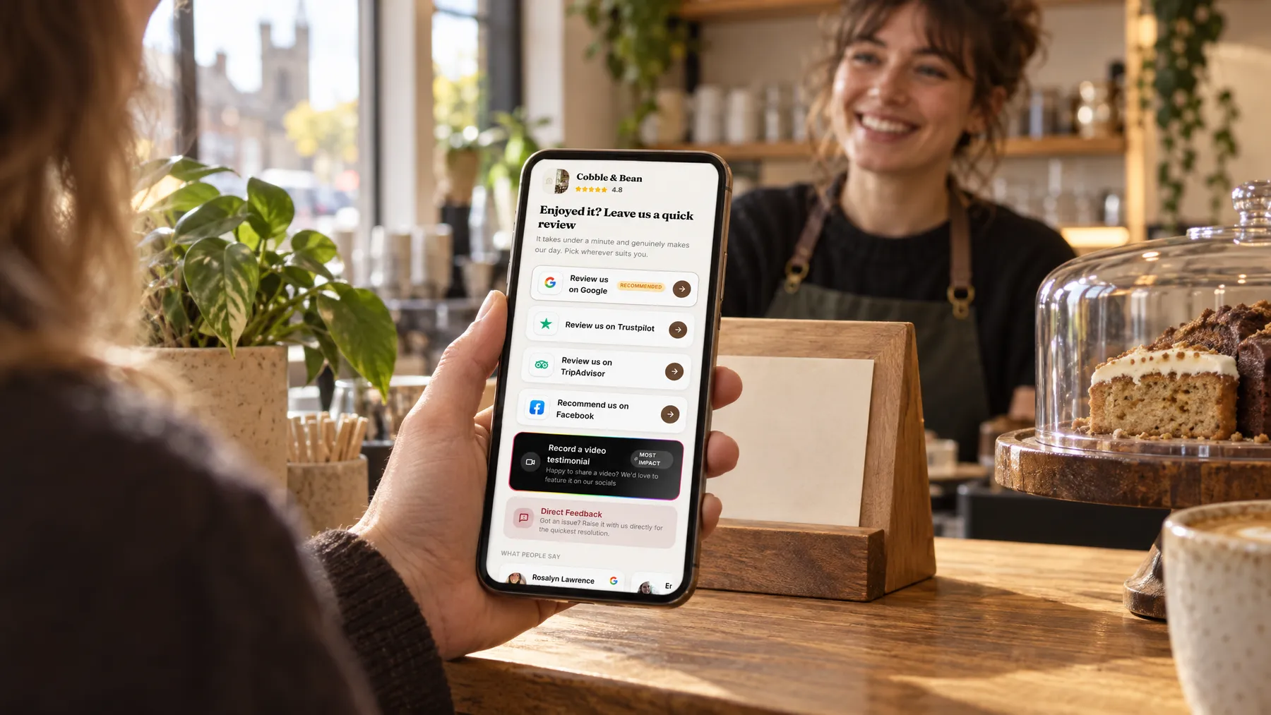 A customer holds up a phone showing a café’s review page above a wooden review stand at the counter.