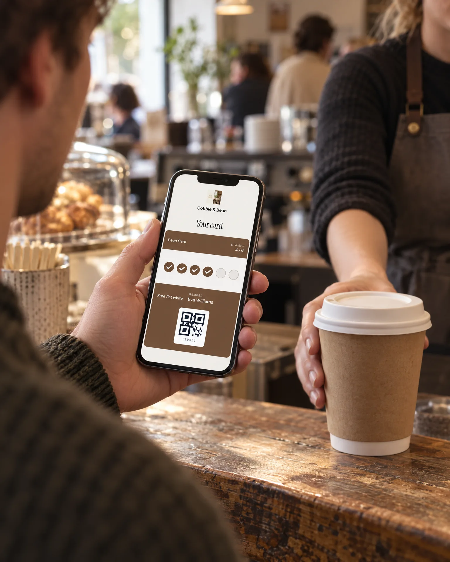A customer showing his Cobble & Bean loyalty card on his phone at the counter